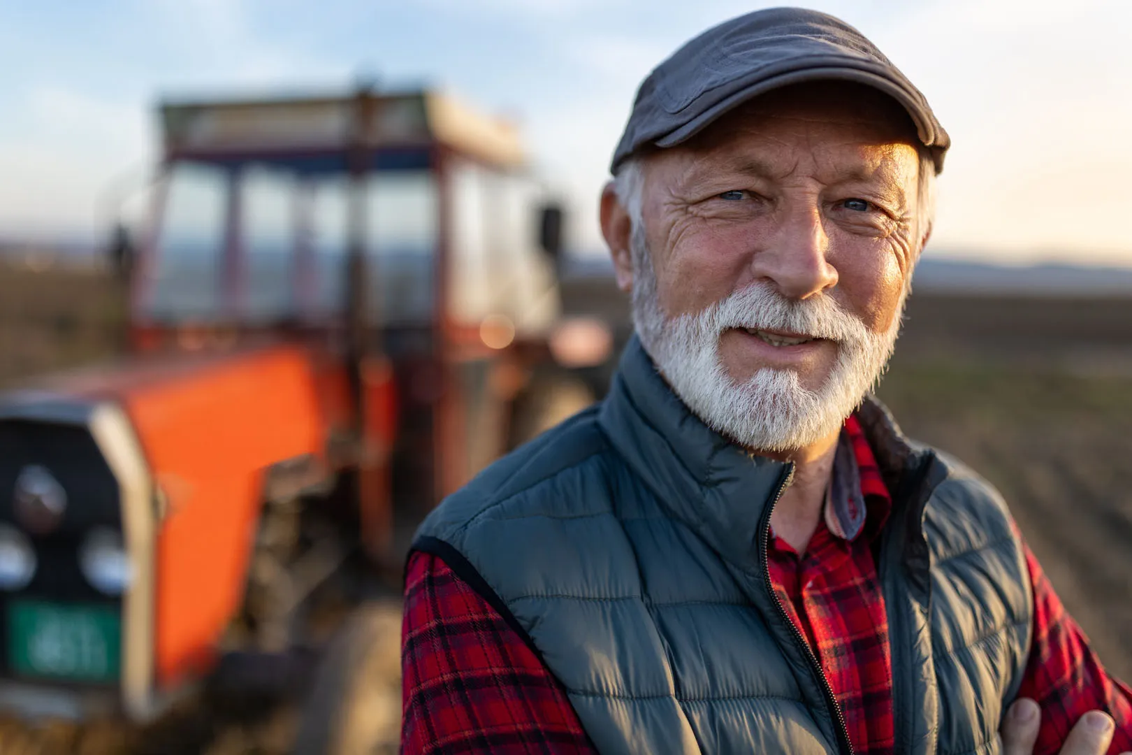 Landwirt mit weißem Bart und Schiebermütze steht vor einem Traktor – Sentaris zu Babyboomern, Rente und Fachkräftemangel
