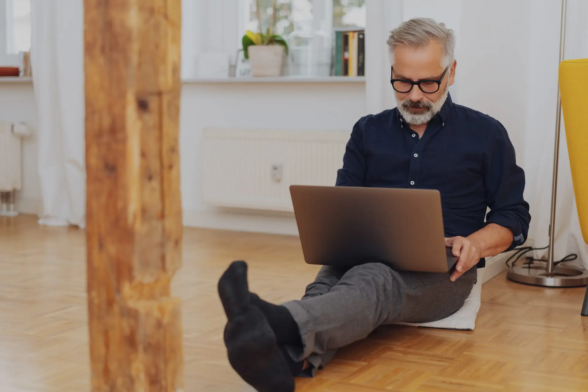Erfahrene Fachkraft mit grauem Bart arbeitet auf dem Wohnzimmerboden am Laptop – vorhandenes Potenzial nutzen mit Sentaris