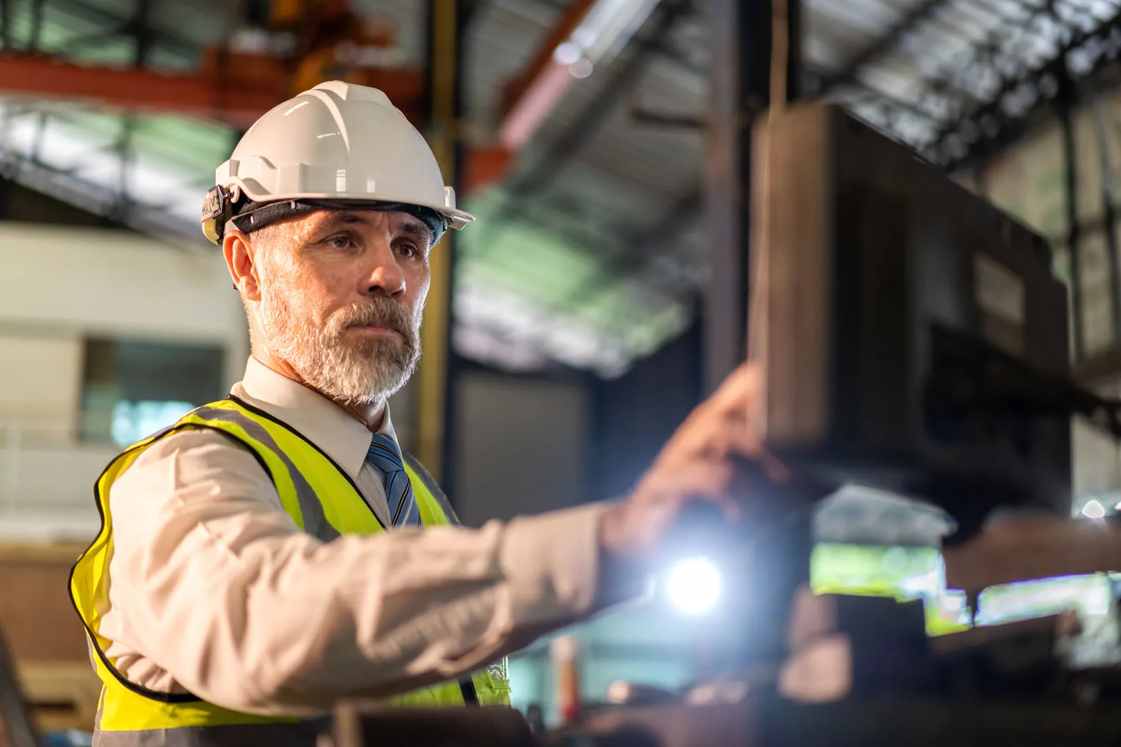 Grauhaariger Ingenieur mit Helm und Warnweste an einer Maschine in der Werkhalle – erfahrene Fachkraft für ein Sentaris-Projekt